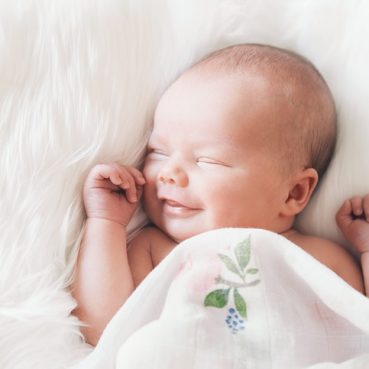Sleeping newborn baby in a wrap on white blanket. Beautiful portrait of little child girl 7 days, one week old. Baby smiling in a dream.